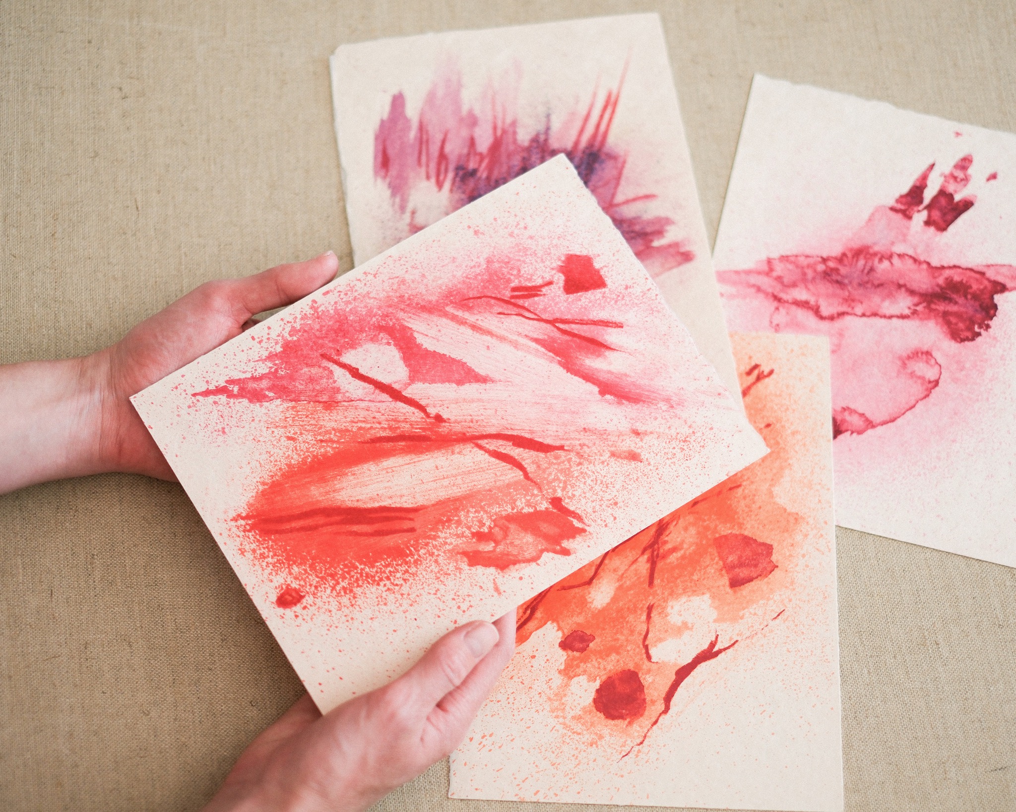 Hands holding coral and pink abstract color studies on paper.