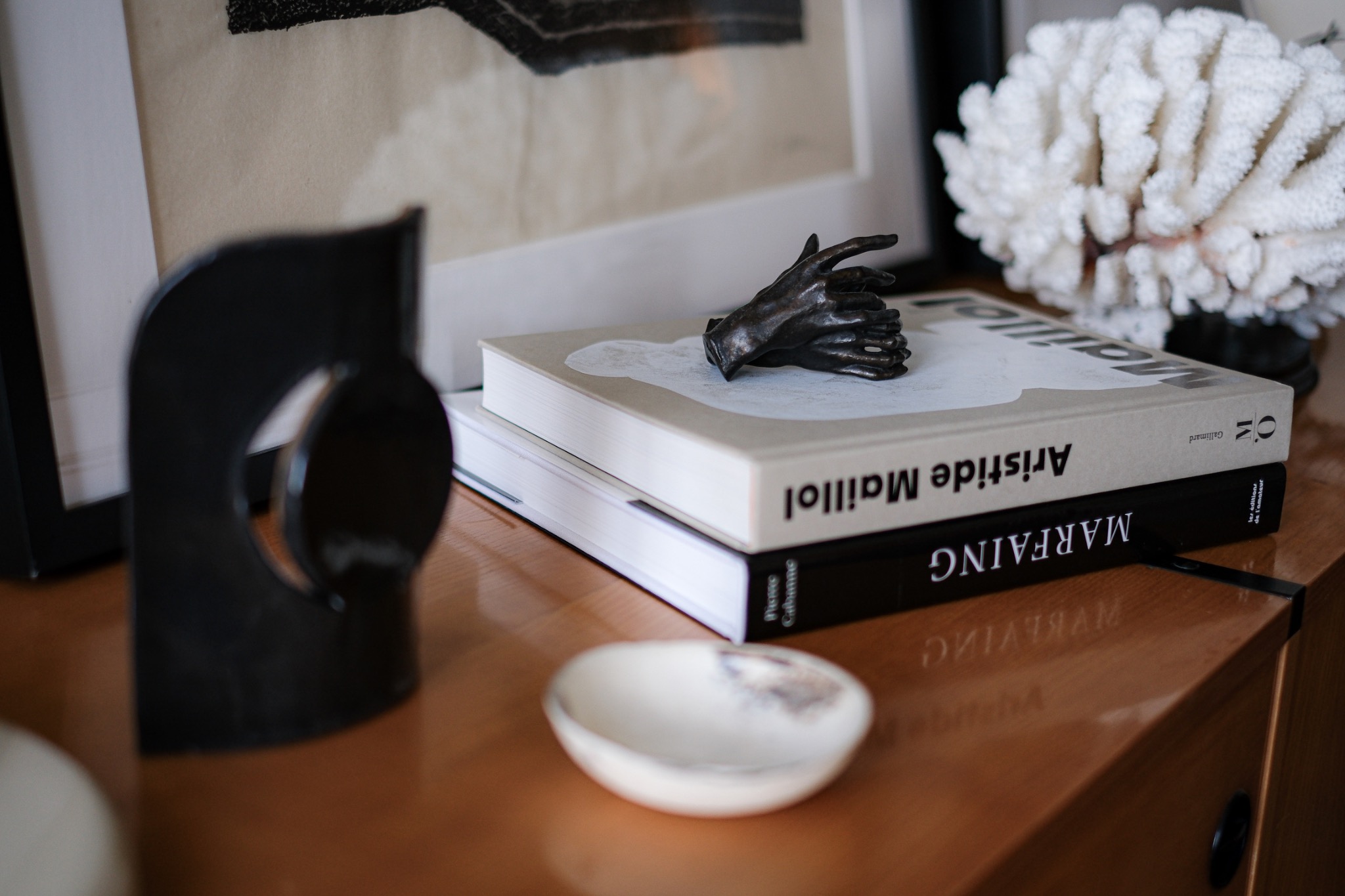 Detail of books, a sculptural bronze hand, coral, and decorative objects arranged on a wooden surface.