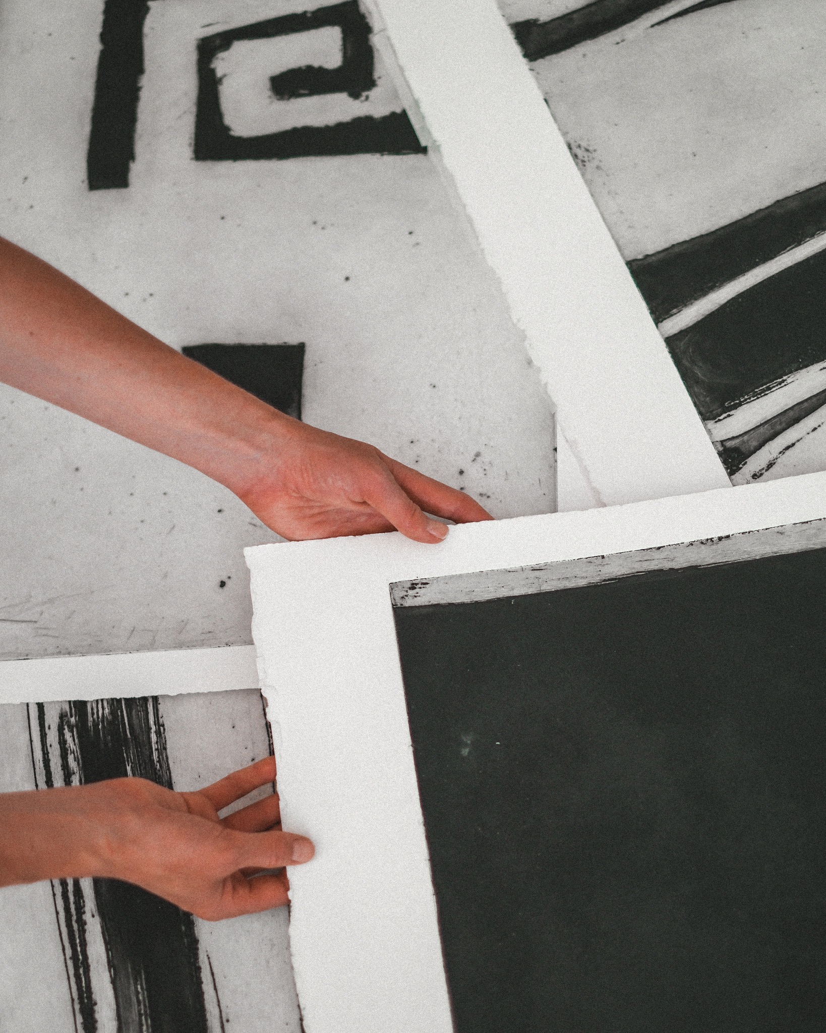 Hands arranging large monochrome art prints on paper.